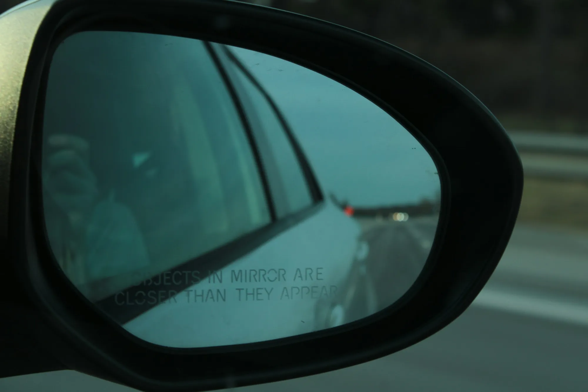 Close-up of a car's side mirror reflecting a blurred highway at dusk