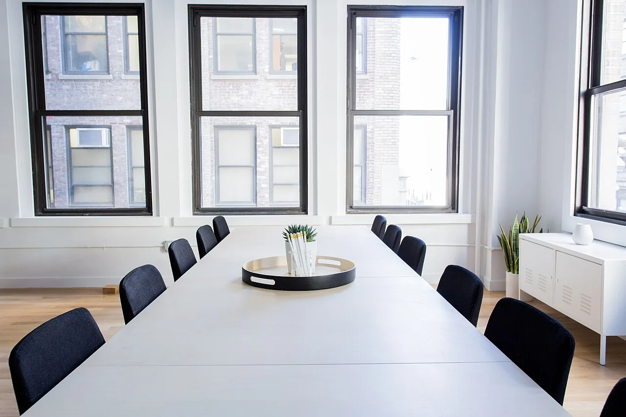 An empty conference table surrounded by chairs and windows