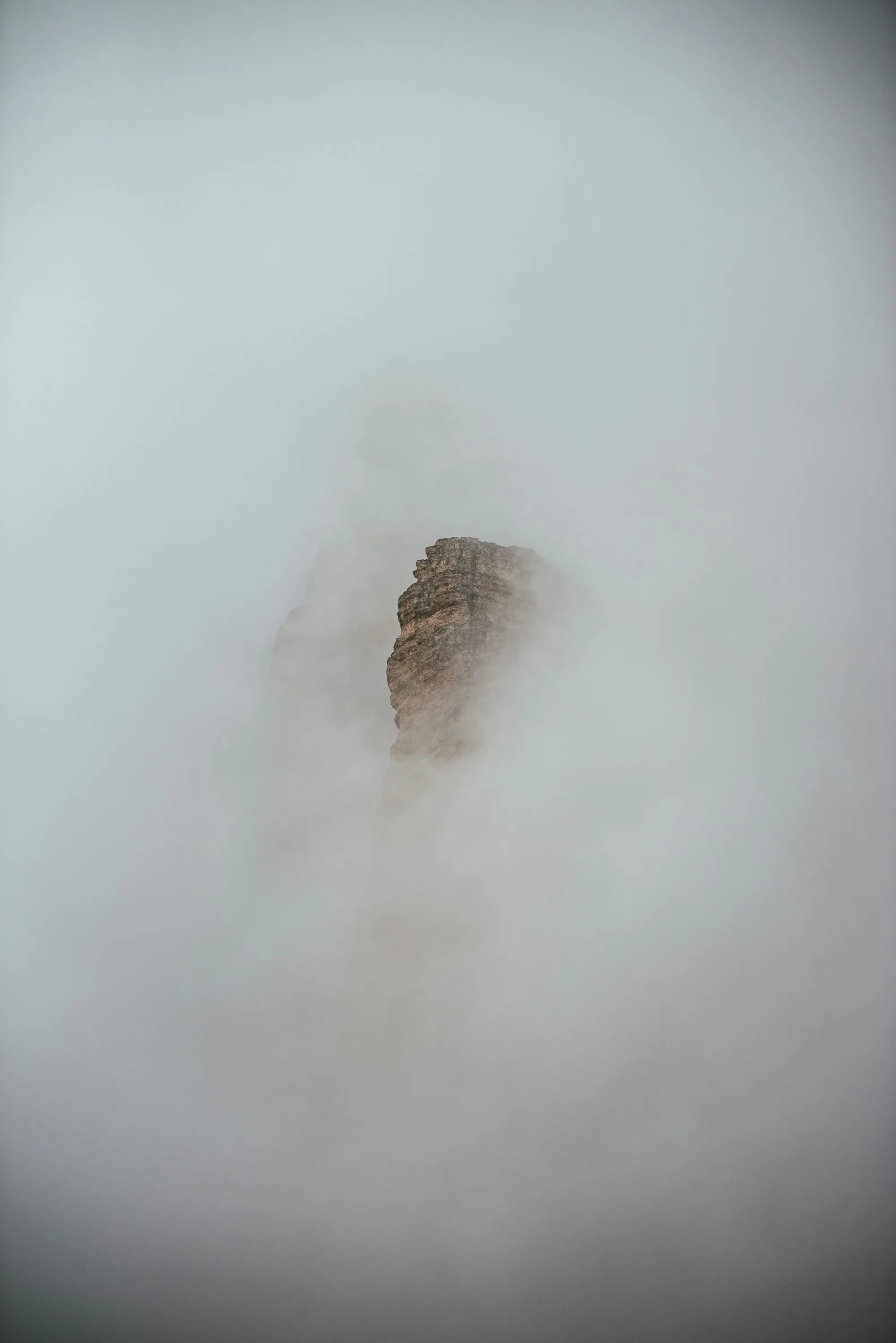 A lone rock emerging from dense mountain fog