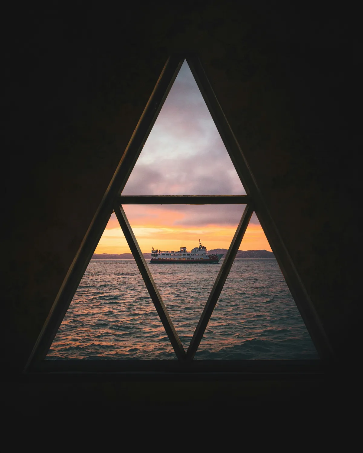 A ferry on the water at sunset, seen through a triangular window