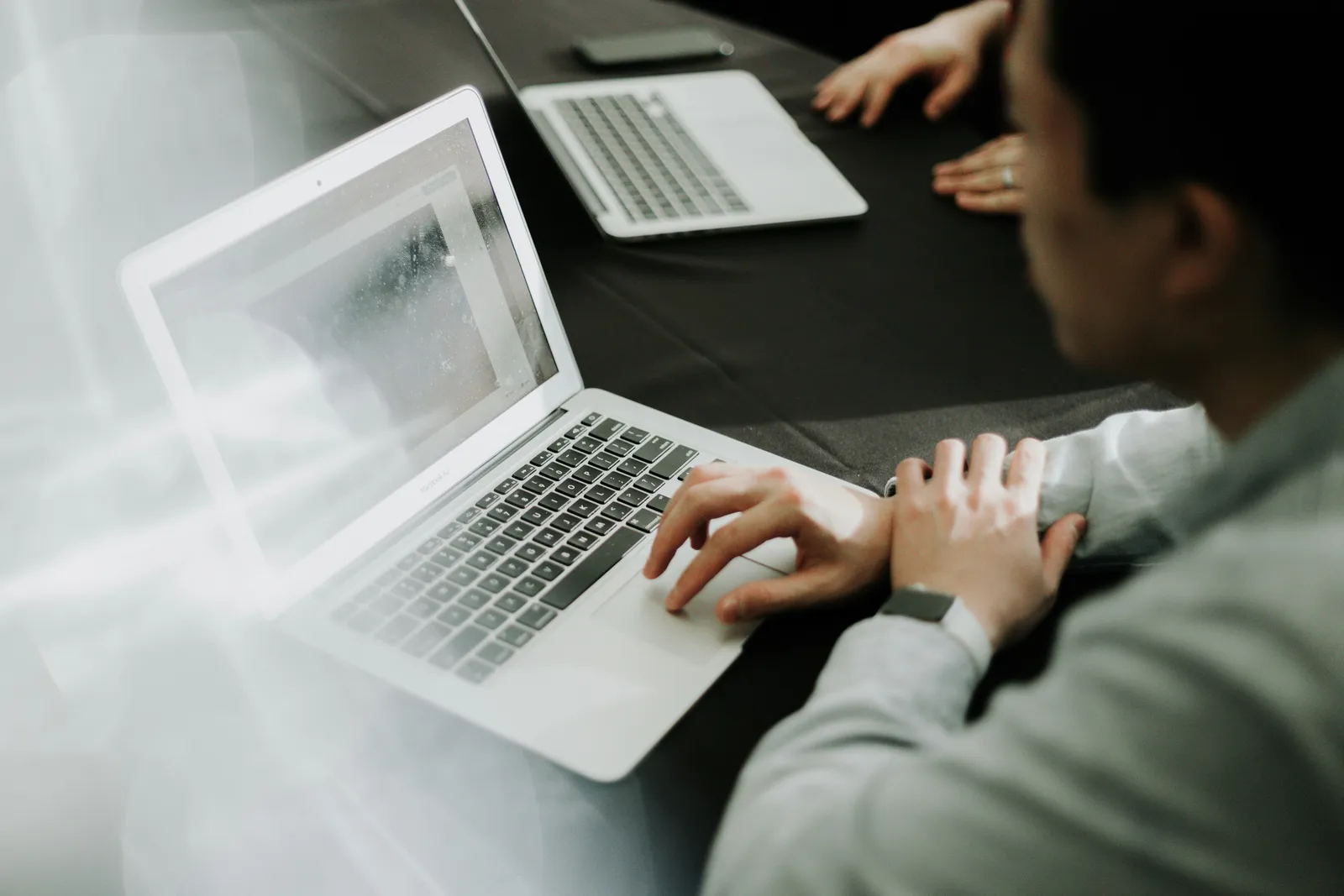 Two people working side by side at a table with laptops