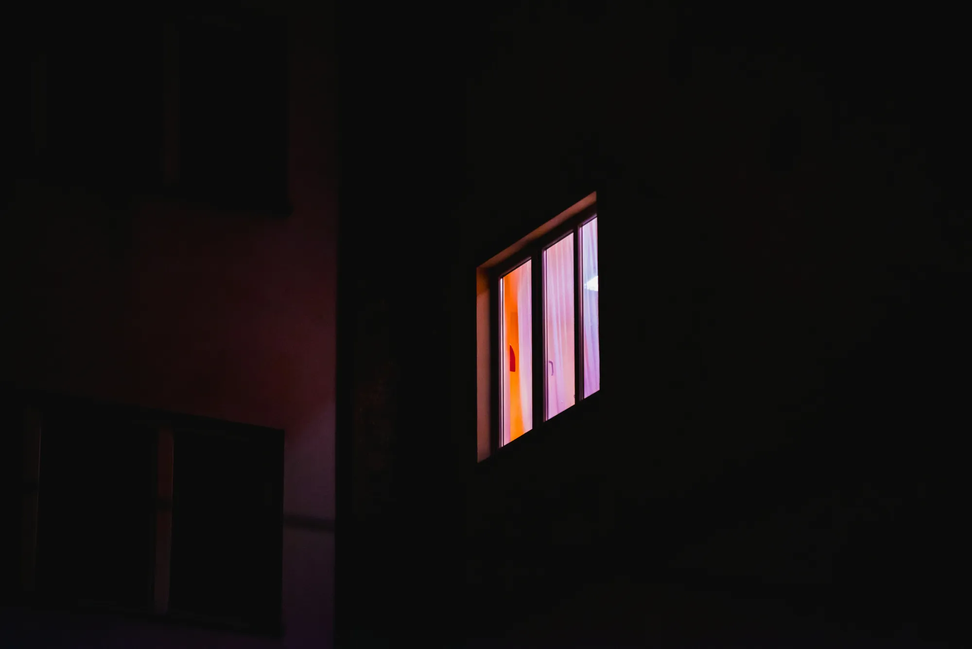 One lit window glowing in an otherwise dark apartment building at night